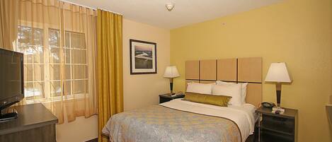 A hotel room with a bed, two bedside tables, a TV, and a window with curtains.