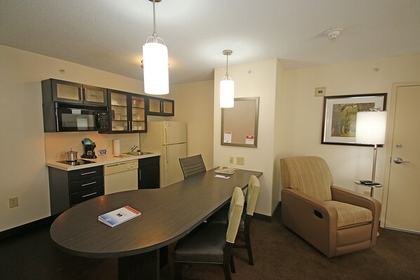 A modern kitchen with a microwave, stove, and cabinets. There is a dining table with chairs and a lamp. - Candlewood Suites Newport News/Yorktown by IHG (Yorktown)