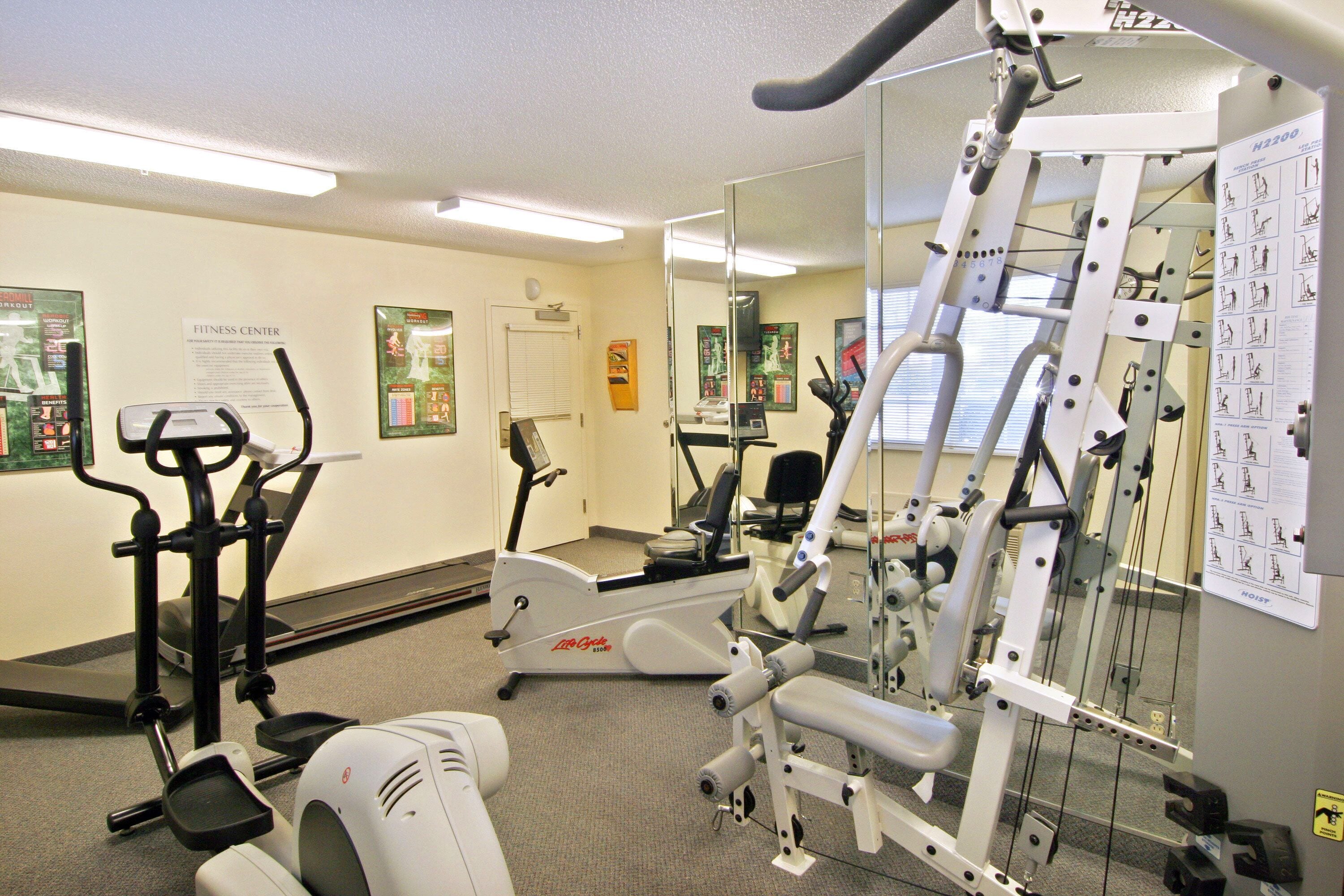 A fitness center with cardio equipment, weight machines, and instructional posters.