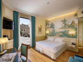 Una camera d'albergo con un letto, una scrivania con una lampada, una sedia, una TV e un affresco sulla parete.