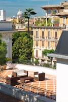 Una terrazza sul tetto con mobili da esterno, vista su un paesaggio urbano che include una cupola e un albero.