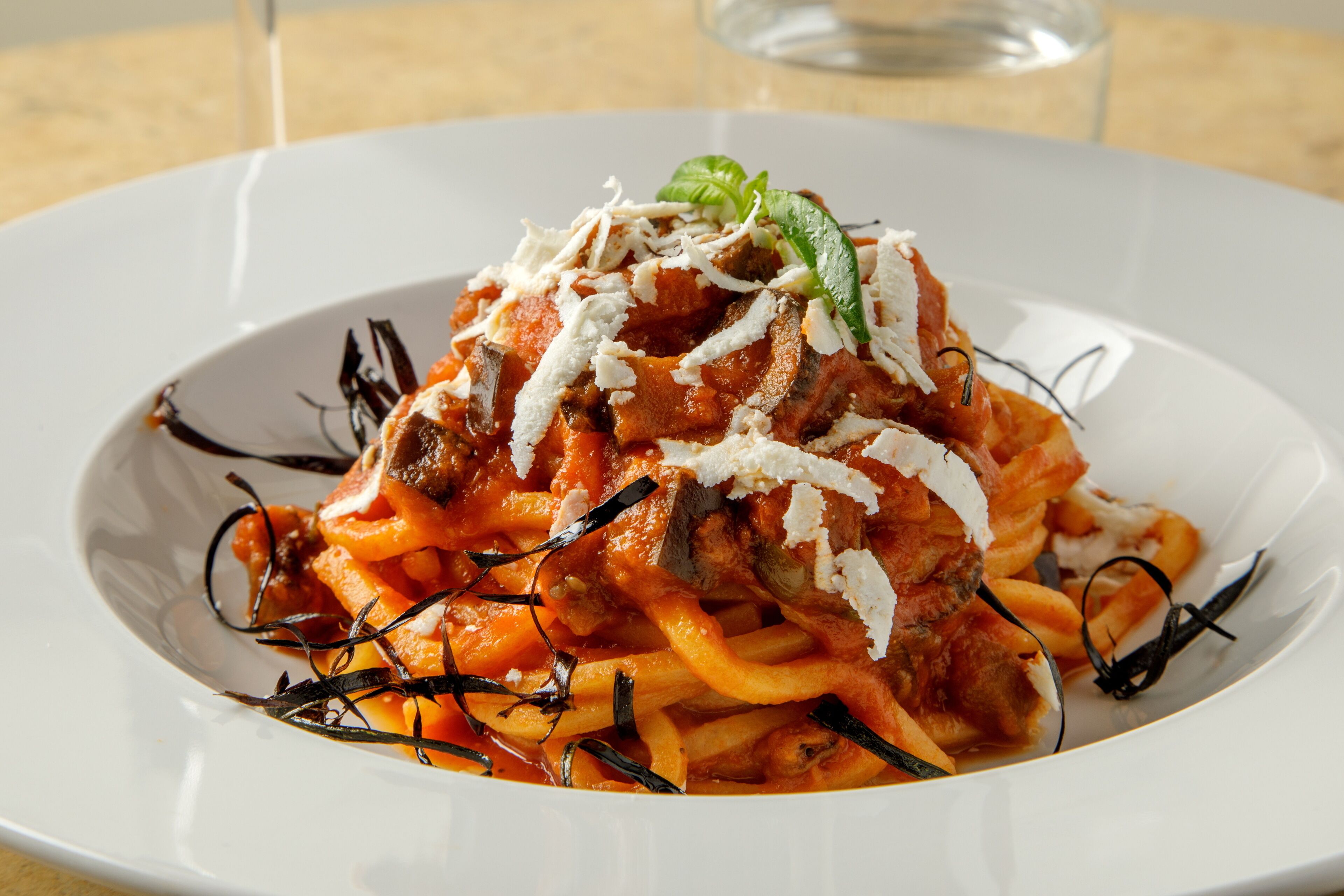 A plate of spaghetti with meatballs in tomato sauce, garnished with cheese and basil.