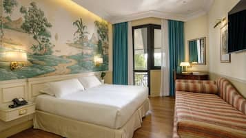 Camera d'albergo con un letto grande, un divano, una scrivania con una lampada e un murale al muro.