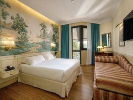 Camera d'albergo con un letto grande, un divano, una scrivania con una lampada e un murale al muro.