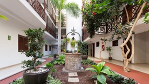 Un cortile con una fontana al centro, circondato da vasi di piante e un sentiero in pietra.
