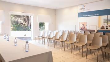 Un salón de conferencias con una larga mesa y sillas, un cartel con texto, y vistas al exterior con vegetación.