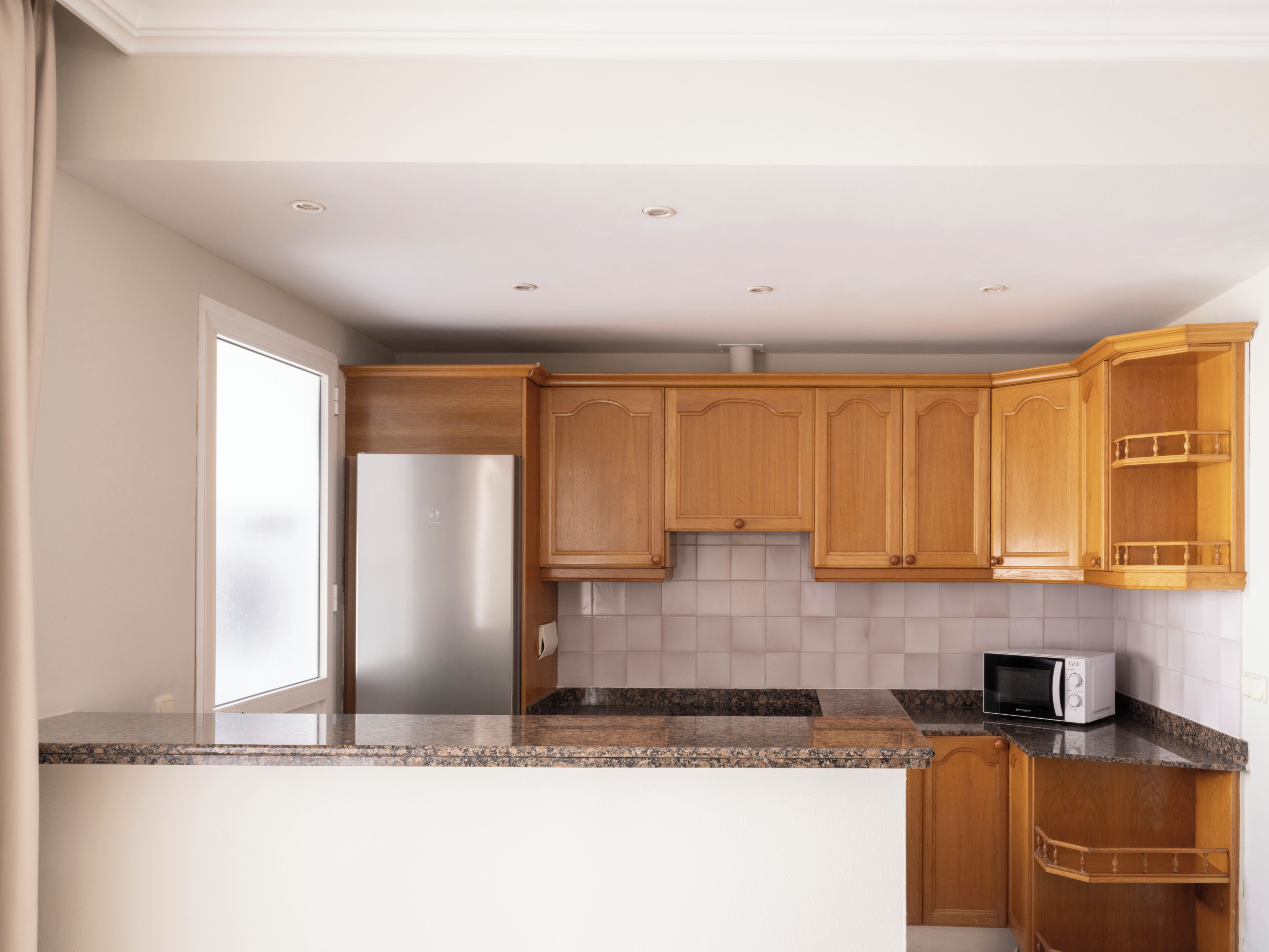 A kitchen with wooden cabinets, a stainless steel refrigerator, a microwave, and a granite countertop.
