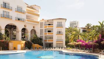 A hotel with a swimming pool, multiple balconies, and a garden area with lounge chairs.