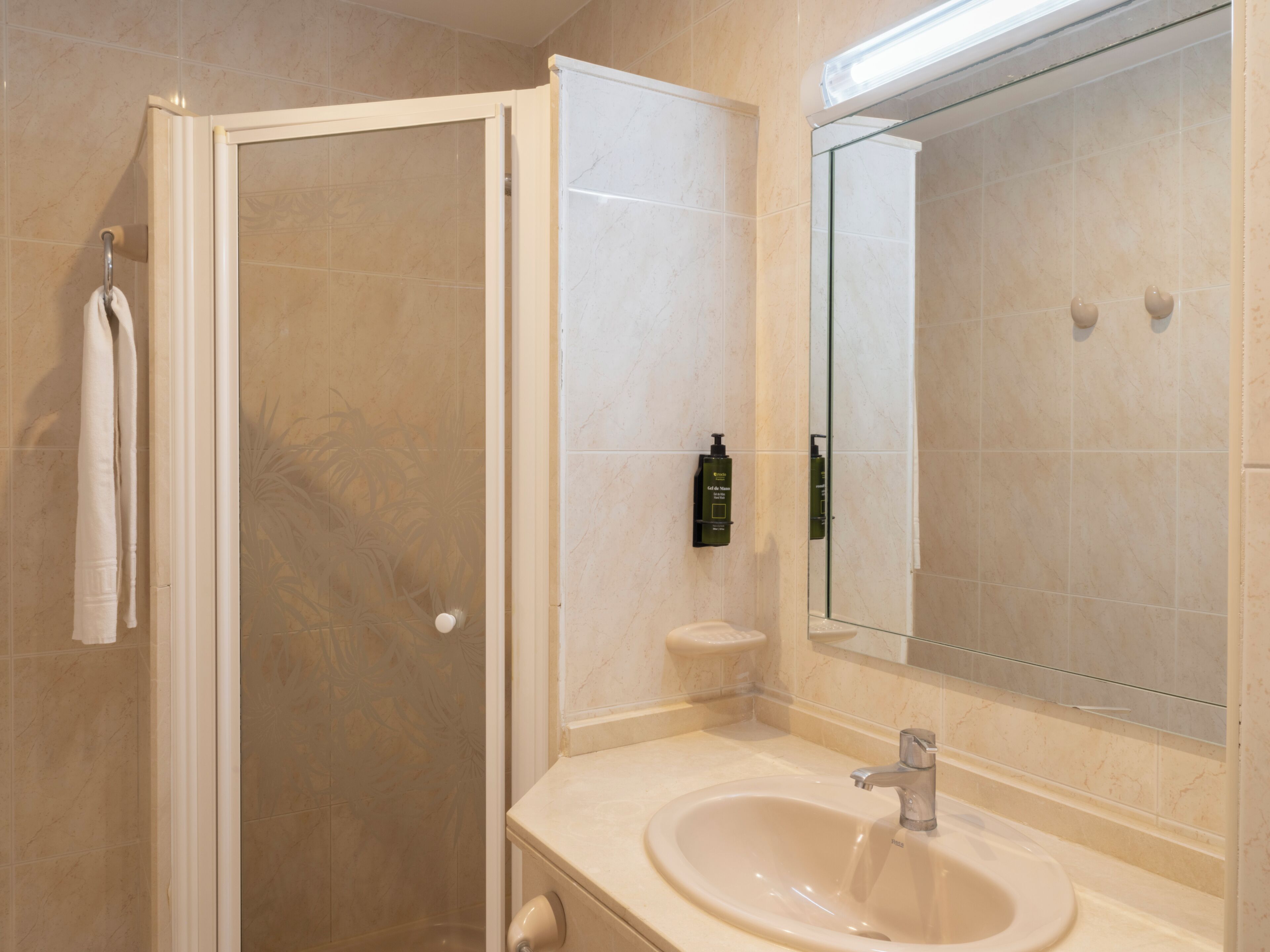 Un baño con ducha, lavamanos, espejo y toallero.