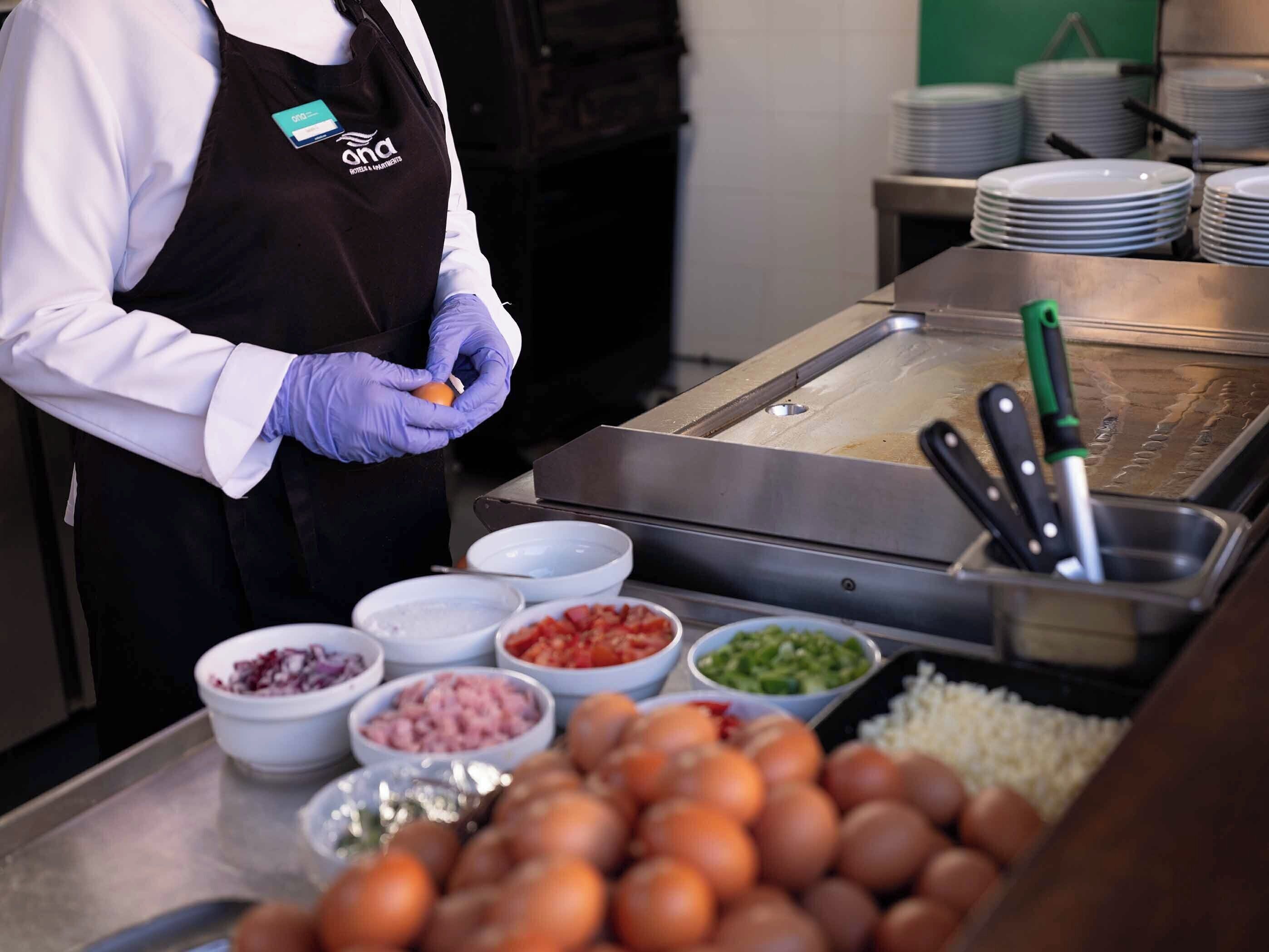 A person in a uniform preparing food at a buffet station with various food items and utensils.