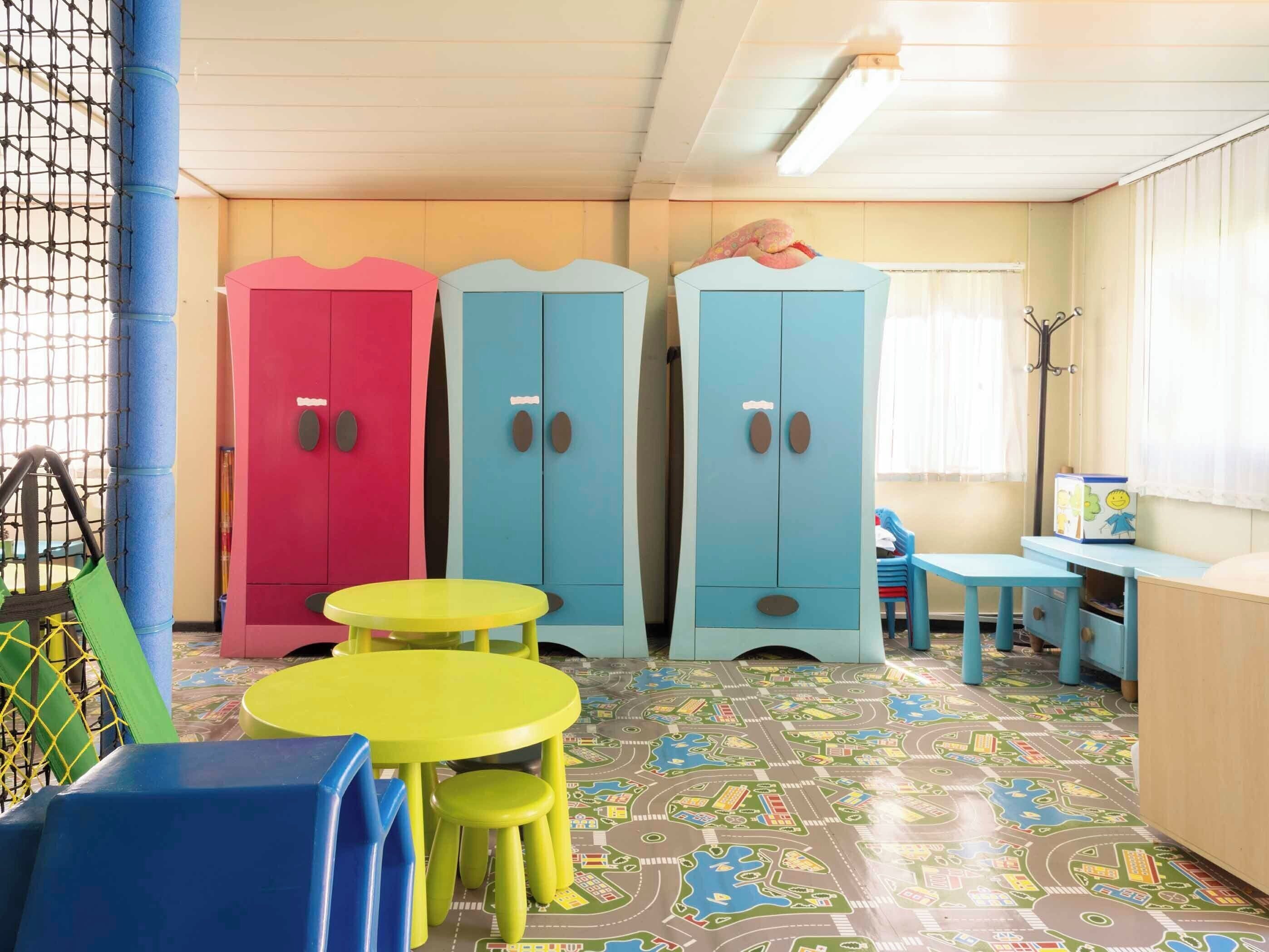 Un salón infantil con armarios de colores, una mesa de juegos y un suelo con diseño de paisaje urbano.