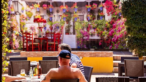 An outdoor dining area with wicker chairs and tables, a brick wall, and hanging flower baskets. - Ona Alanda Club Marbella (Marbella)