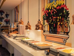 A buffet setup with various food items, hanging pendant lights, and a decorative wall with a floral motif. - Ona Alanda Club Marbella (Marbella)