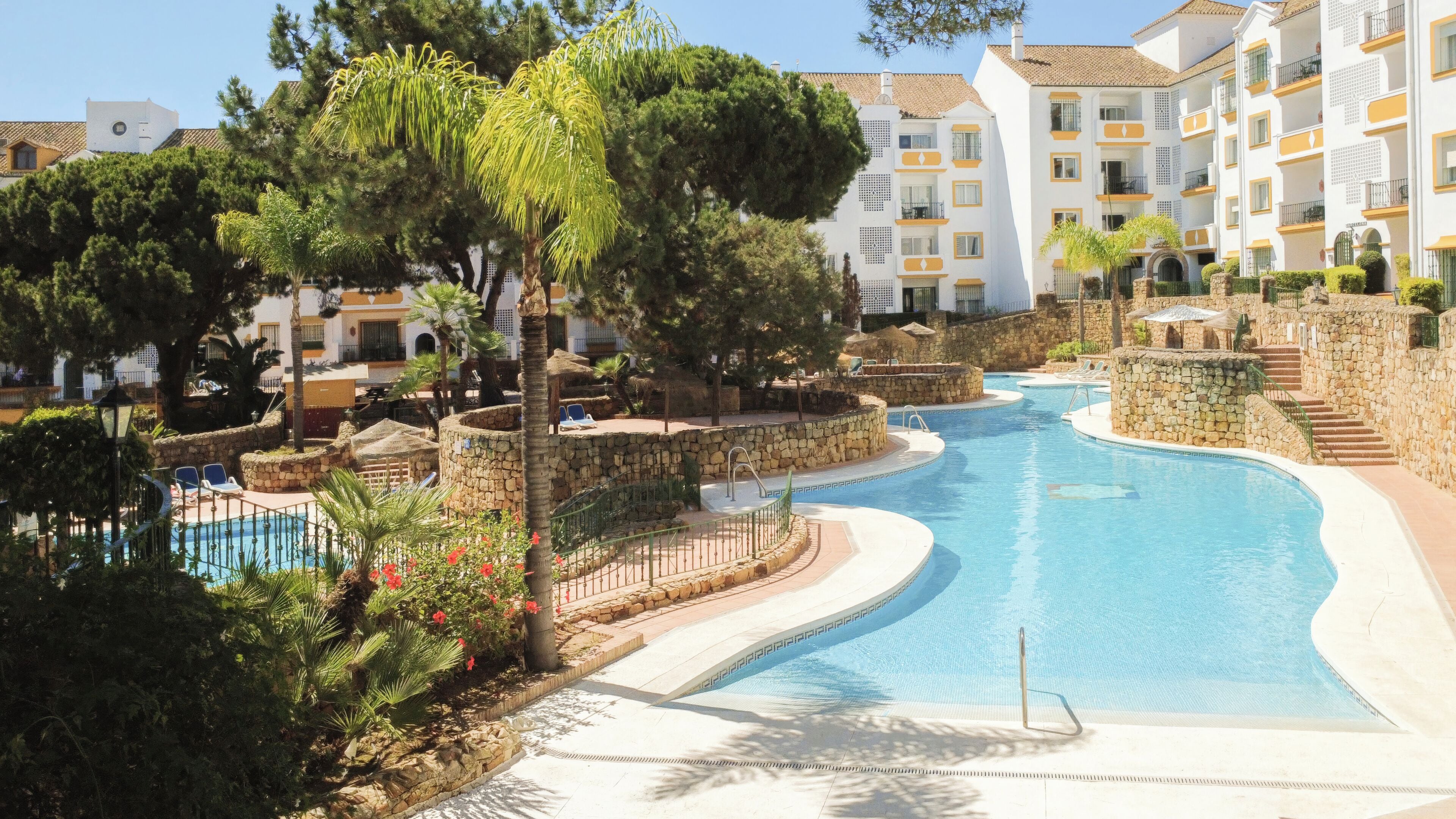 A resort with a swimming pool, stone walls, and multiple-story buildings with balconies.