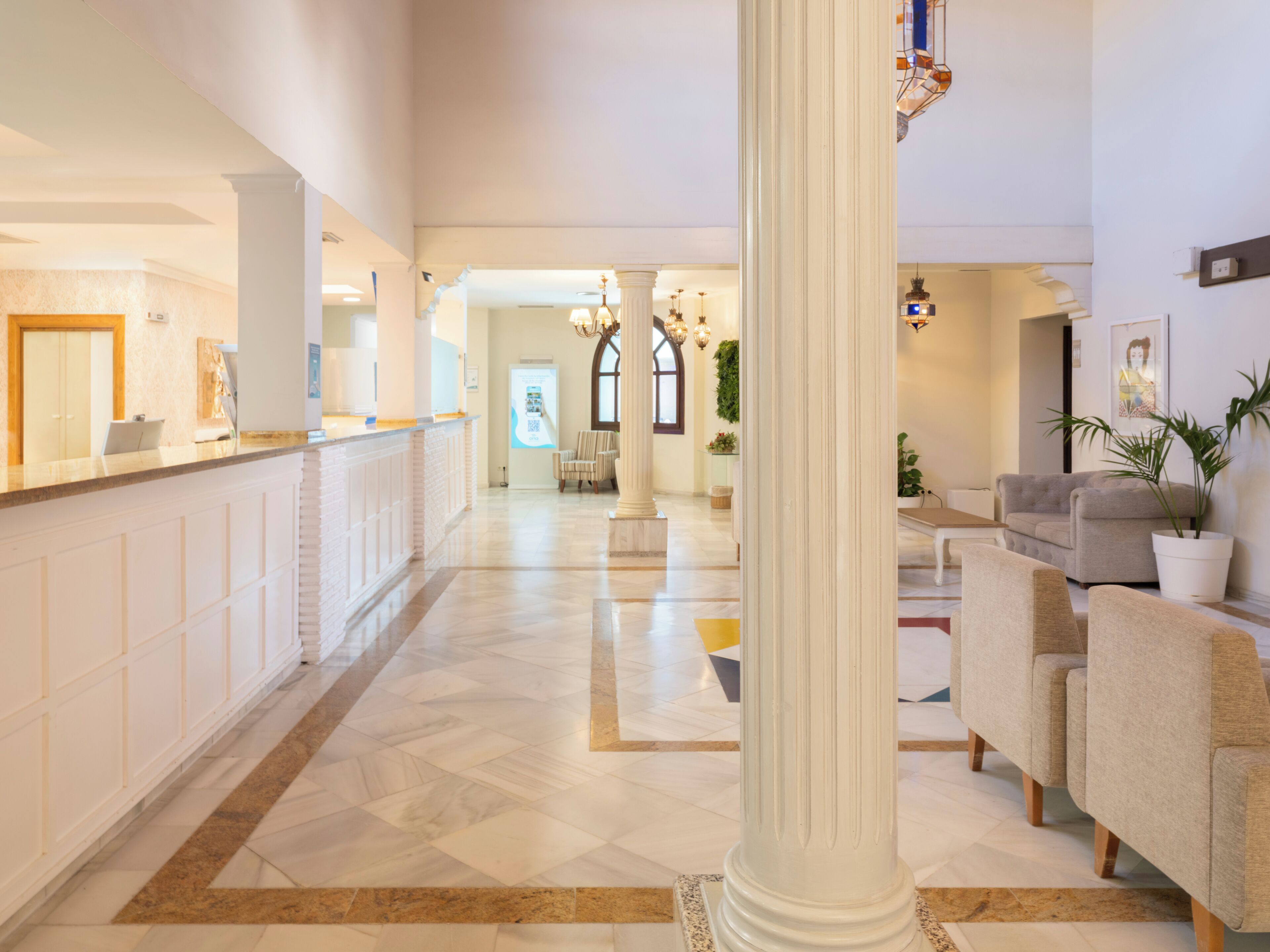 A hotel lobby with a reception desk, seating area, and a large column.