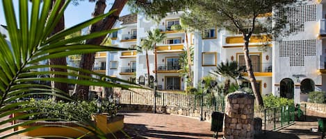 A courtyard with a stone wall, a palm tree, and a building with balconies and a sign reading "ALMERIA".