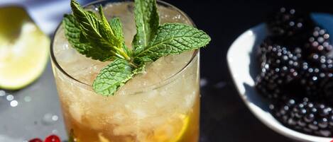 A glass of iced beverage with mint leaves, a slice of lime, and a bowl of blackberries in the background.