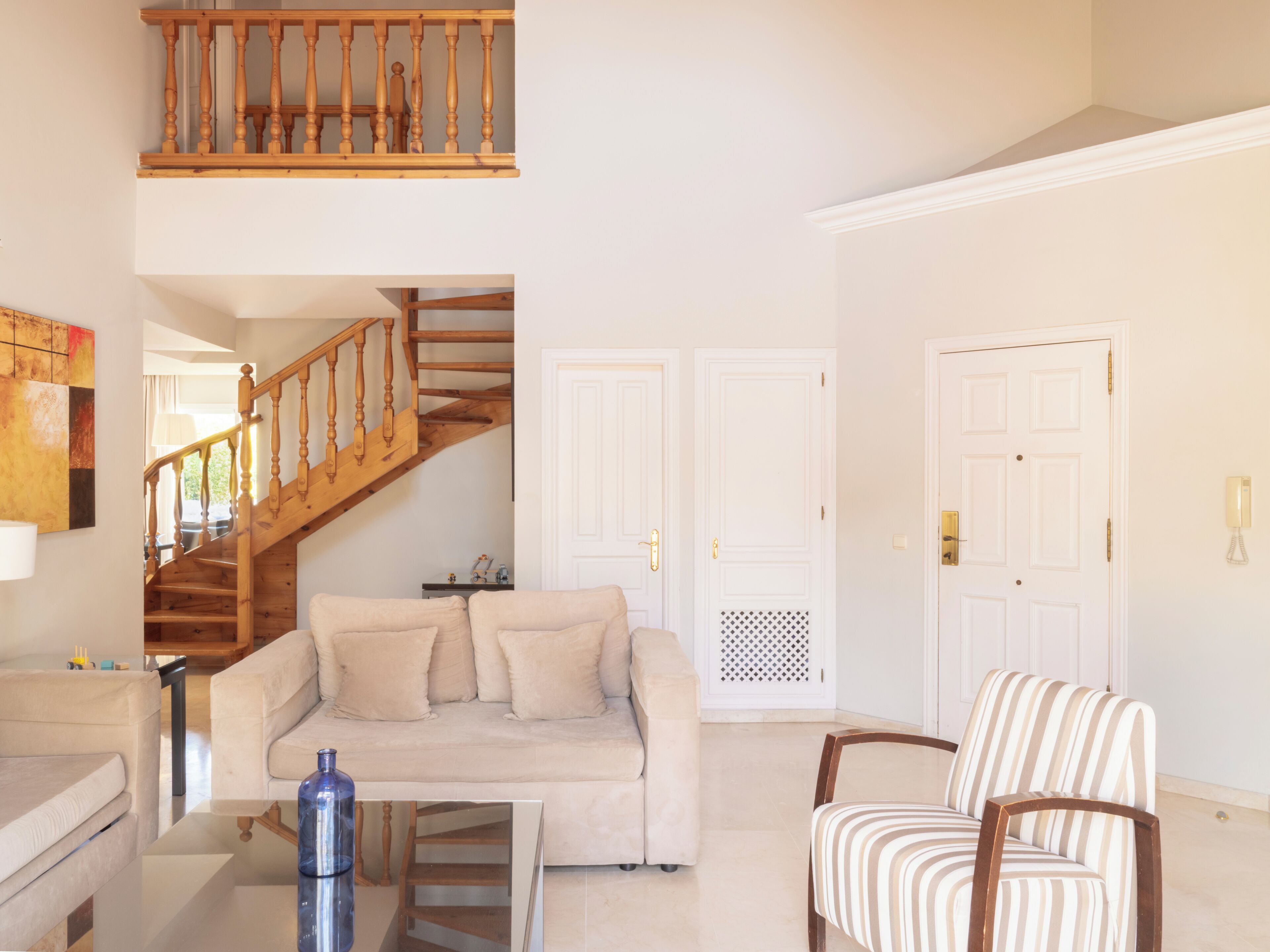 Una sala de estar con una escalera de madera, un sofá, un sillón a rayas y una mesa de centro.