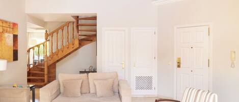Una sala de estar con una escalera de madera, un sofá, un sillón a rayas y una mesa de centro.