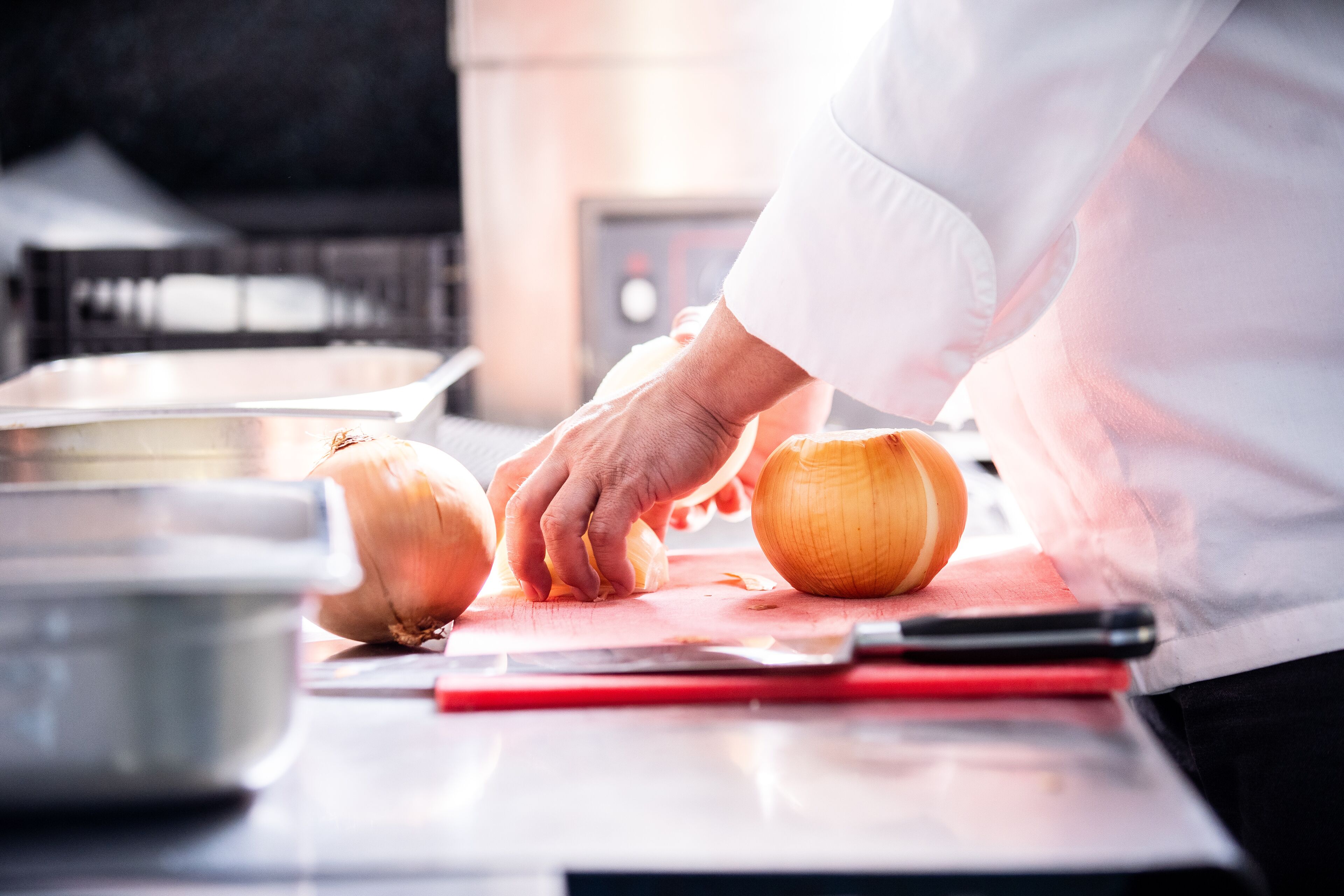 Un chef corta una cebolla sobre una tabla de cortar en una cocina.