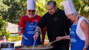 Three people cooking outdoors with a large pan on a portable stove.