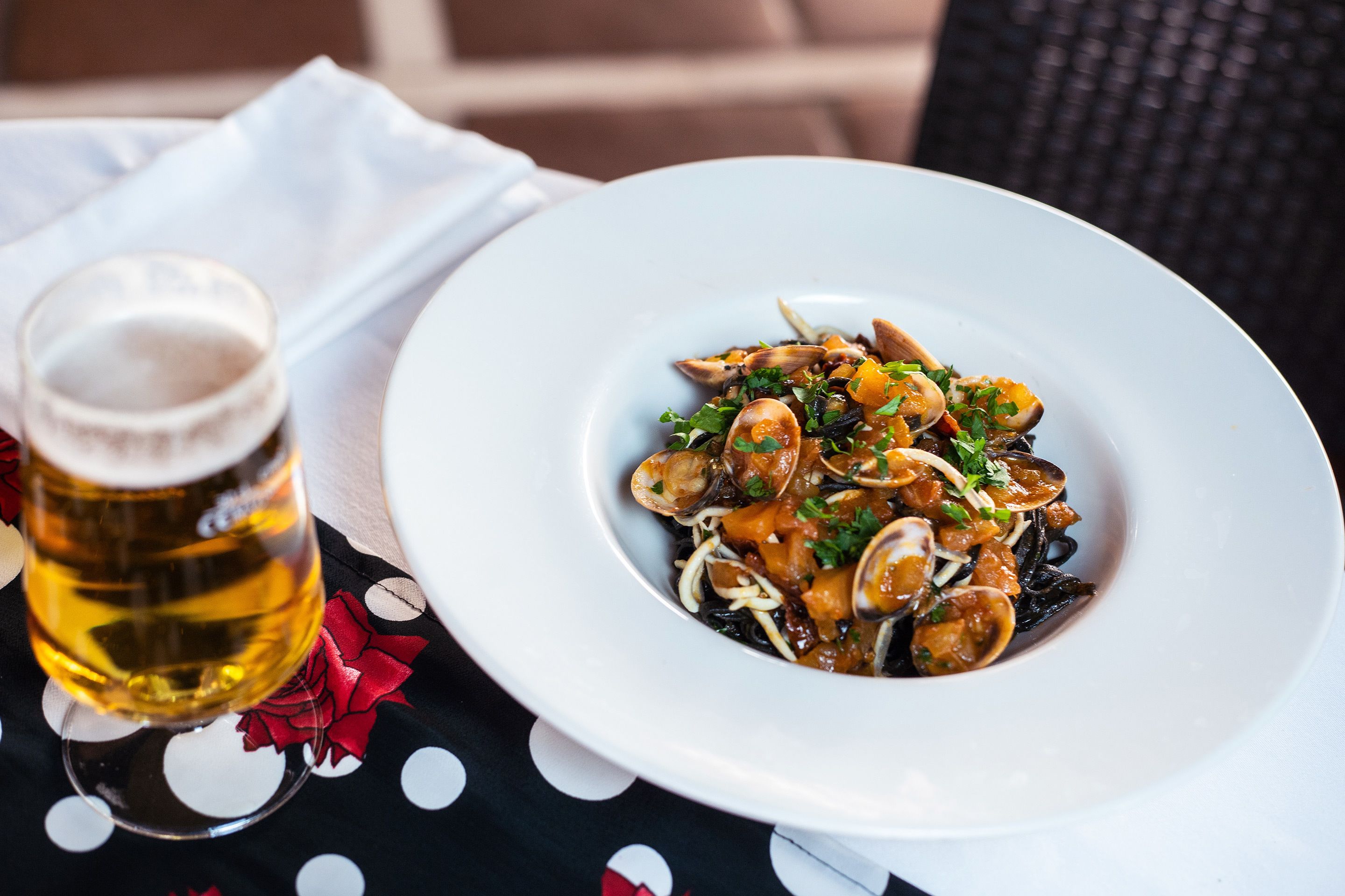 Un plato de pasta con mariscos y una cerveza sobre una mesa con mantel de lunares.