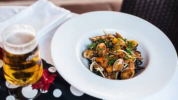 Un plato de pasta con mariscos y una cerveza sobre una mesa con mantel de lunares.