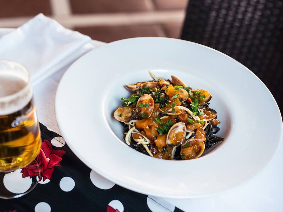 Un plato de pasta con mariscos y una cerveza sobre una mesa con mantel de lunares.