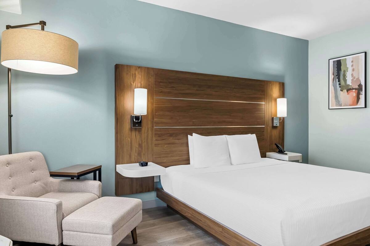 A hotel room with a large bed, a chair, a bedside table, a lamp, and a wall-mounted light fixture.