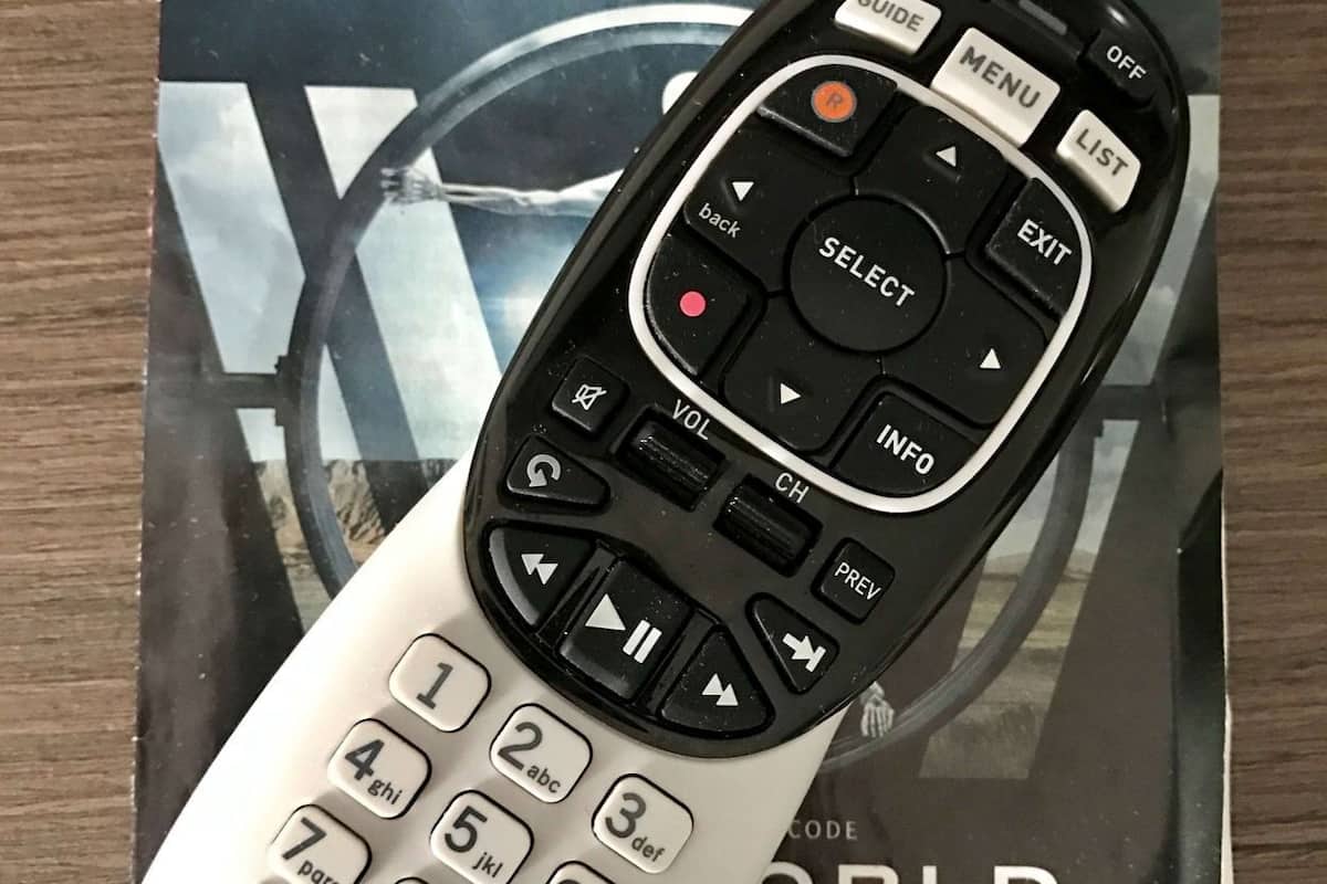 A remote control and a guide for HBO World on a wooden surface.