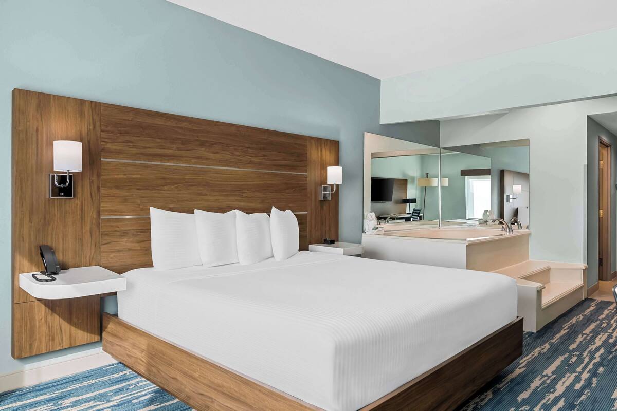 A hotel room with a large bed, bedside tables, a mirror, and a bathroom with a sink and mirror.