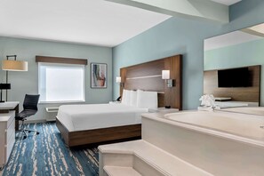 A hotel room with a bed, a desk, a chair, a large window, a painting, a headboard, a TV, and a bathtub.