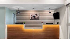 A reception desk with a cityscape artwork above, two pendant lights, and a flat-screen TV on the wall. - Best Western Executive Inn (Seagoville)