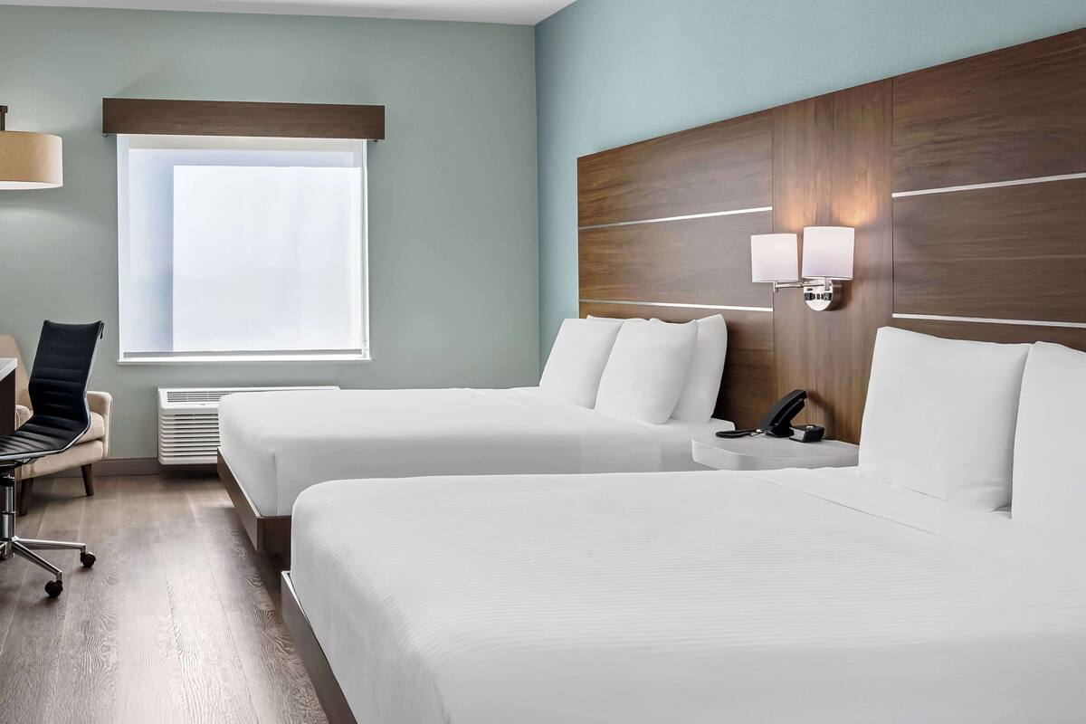 A hotel room with two beds, a desk, a chair, and a window.