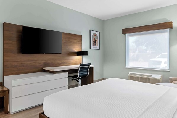A modern hotel room with a bed, a desk, a chair, a TV, and a window with a view of the outside.