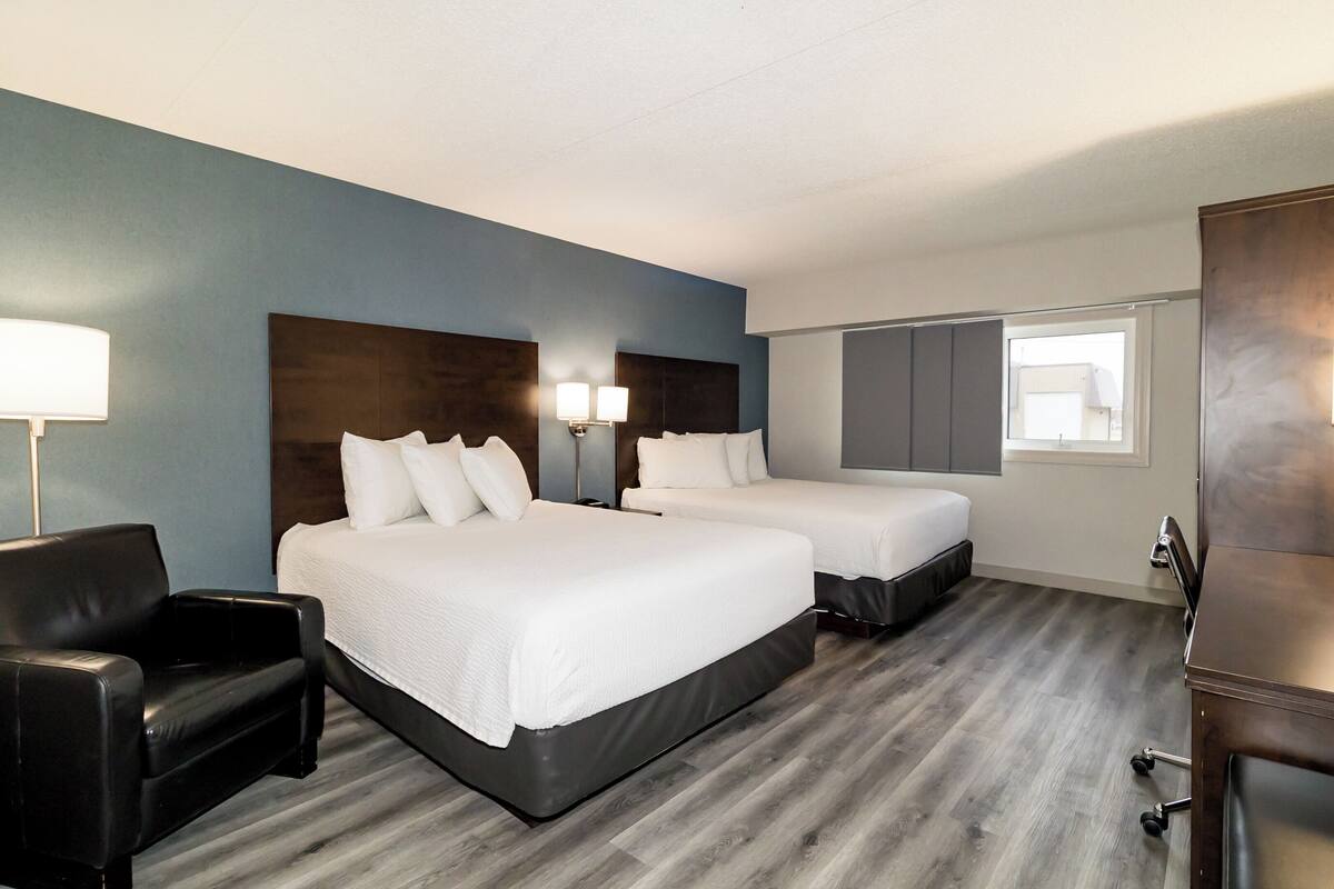 Une chambre d’hôtel avec deux lits, un bureau, une chaise et une fenêtre.
