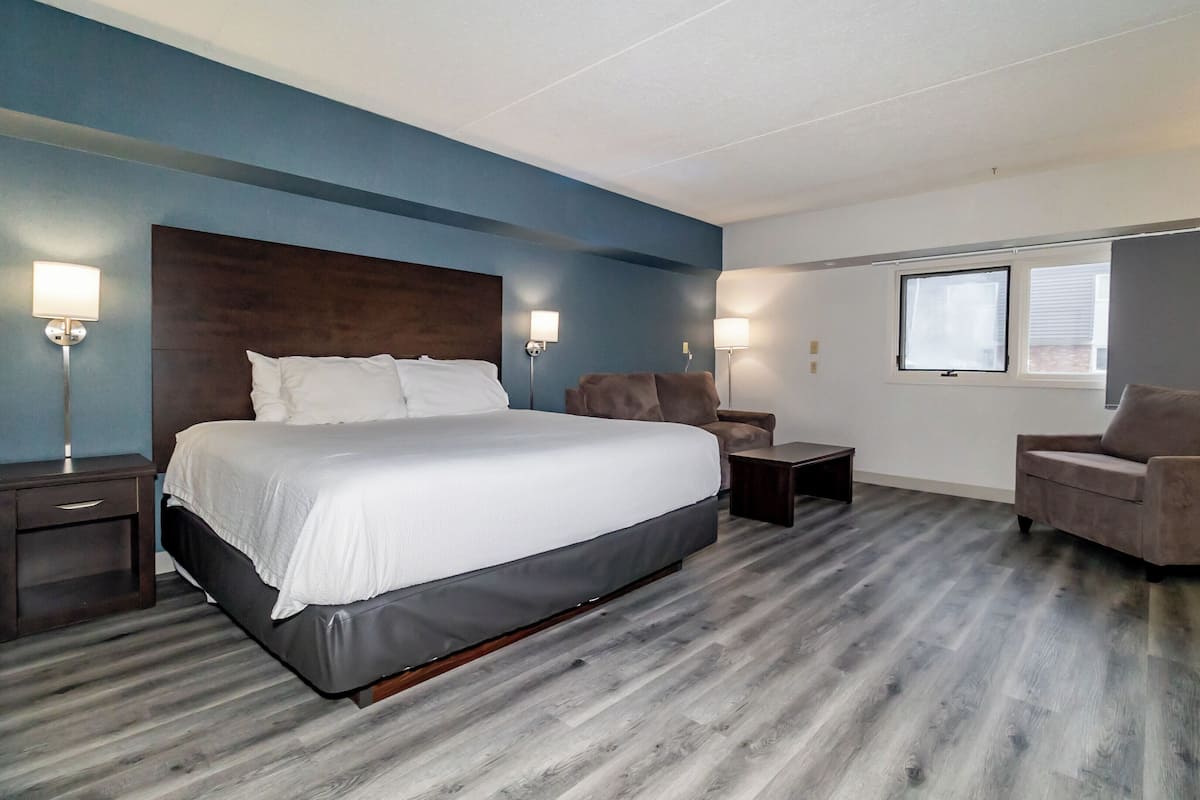 Une chambre d’hôtel moderne avec un grand lit, deux tables de chevet, un canapé et une fenêtre.