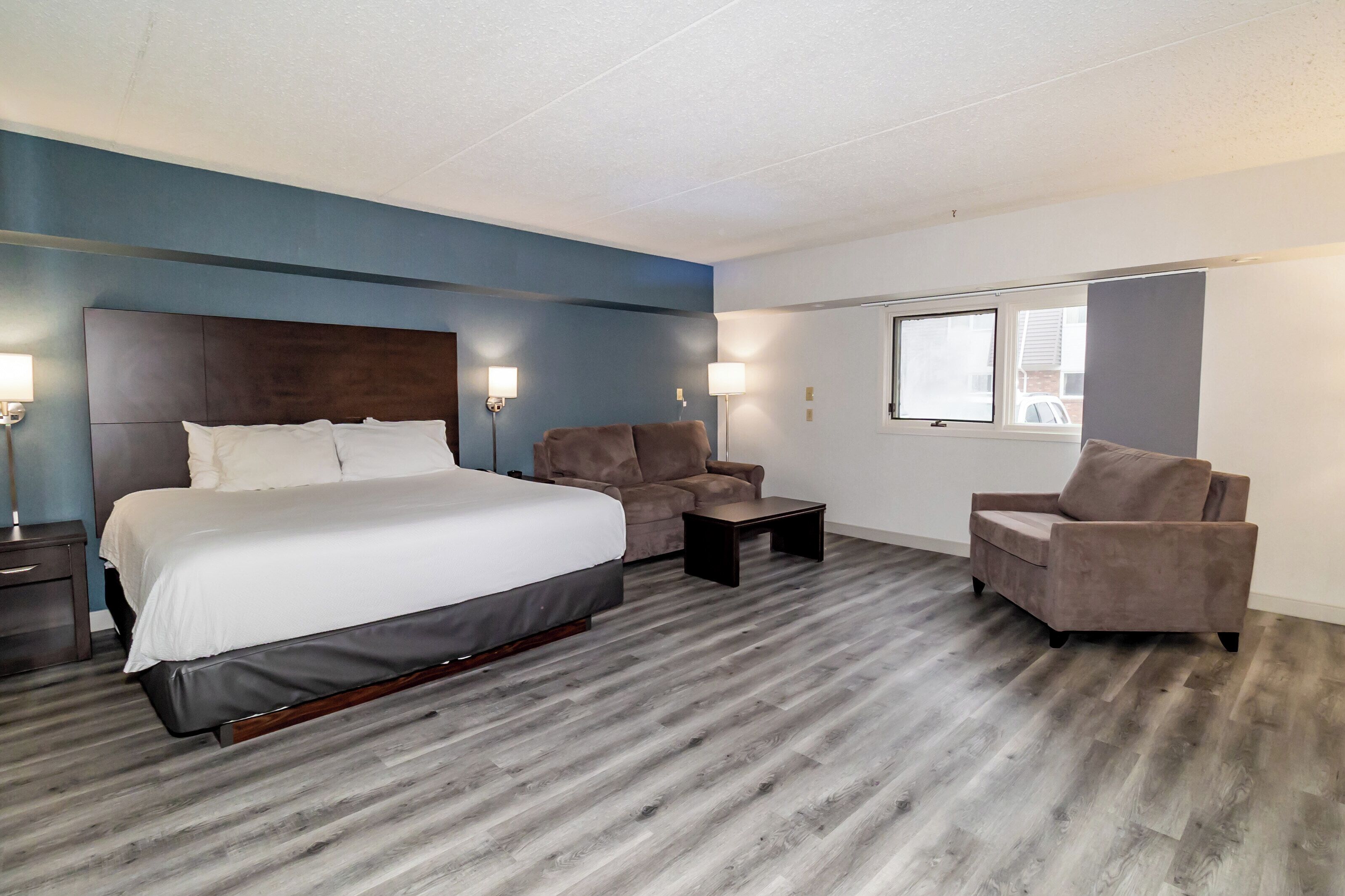 Una habitación de hotel con una cama grande, dos sillones, una mesita y un ventanal.