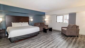 Una habitación de hotel con una cama grande, dos sillones, una mesita y un ventanal.