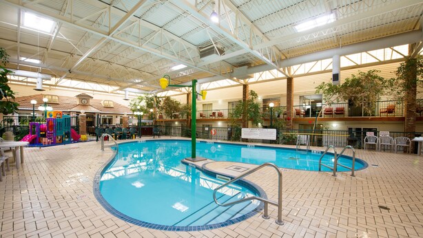 An indoor swimming pool with a tiled floor, a green pool ladder, and a play area with colorful slides. - Victoria Inn Hotel & Convention Centre Brandon (Brandon)