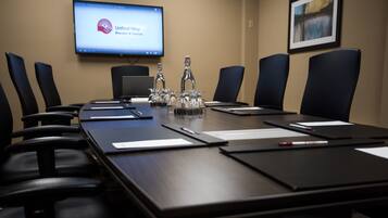 Une salle de conférence avec une longue table, des chaises noires, un ordinateur portable, des bouteilles en verre et un écran affichant un logo.
