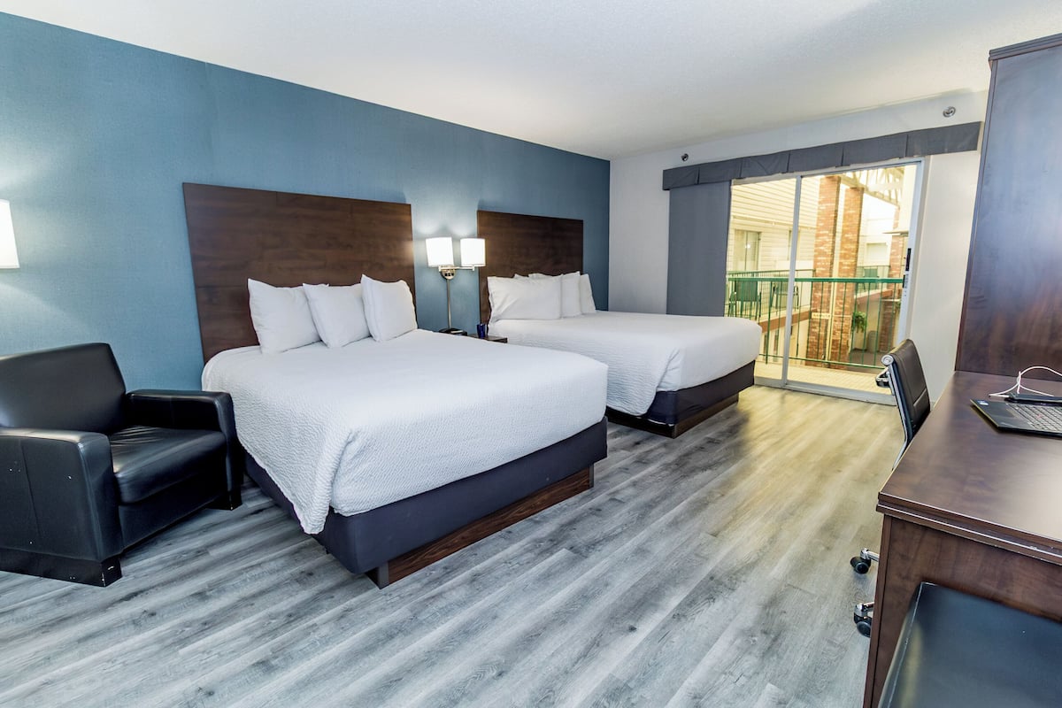 Une chambre d’hôtel avec deux lits, un bureau, une chaise et un balcon avec vue.