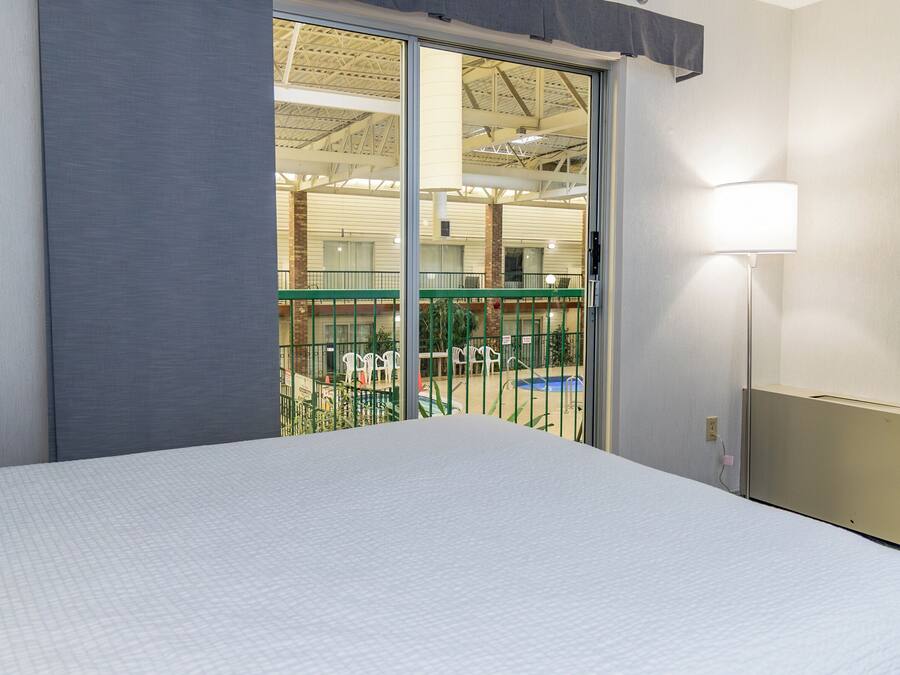 A hotel room with a large bed, a sliding glass door leading to an outdoor area with a pool and chairs.