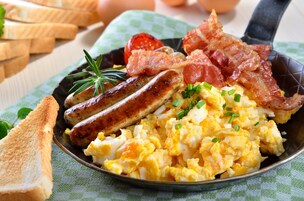 Un plato de desayuno con huevos revueltos, salchichas, tocino, tostadas y tomate.