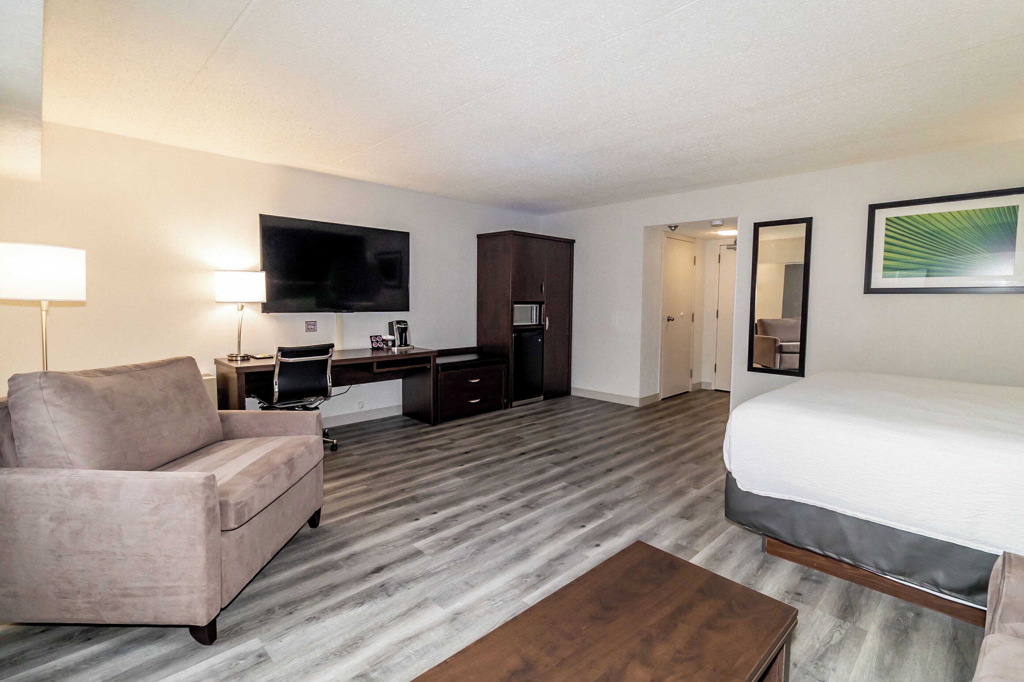 A hotel room with a bed, a desk, a chair, a television, and a wardrobe.
