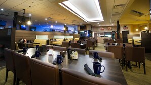 A modern dining area with booths and tables, equipped with blue mugs and napkins, and a visible bar area in the background. - Victoria Inn Hotel & Convention Centre Brandon (Brandon)