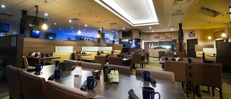A modern dining area with booths and tables, equipped with blue mugs and napkins, and a visible bar area in the background.