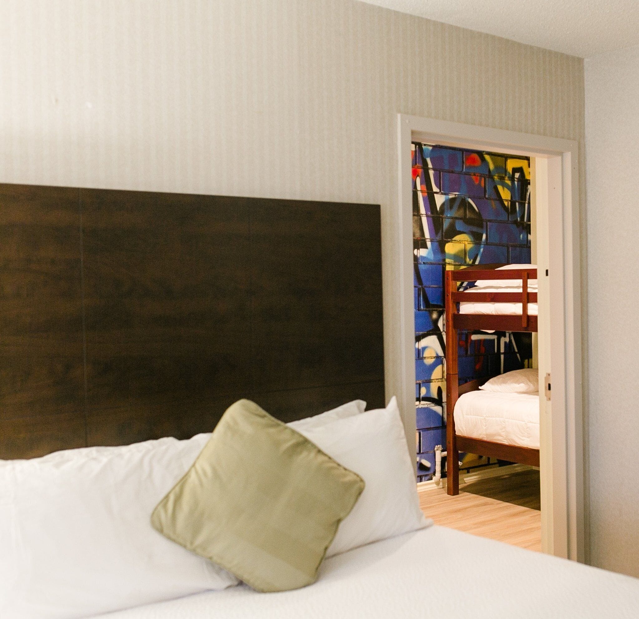 Une chambre d’hôtel avec un lit, une tête de lit en bois et un lit superposé visible à travers une porte ouverte.