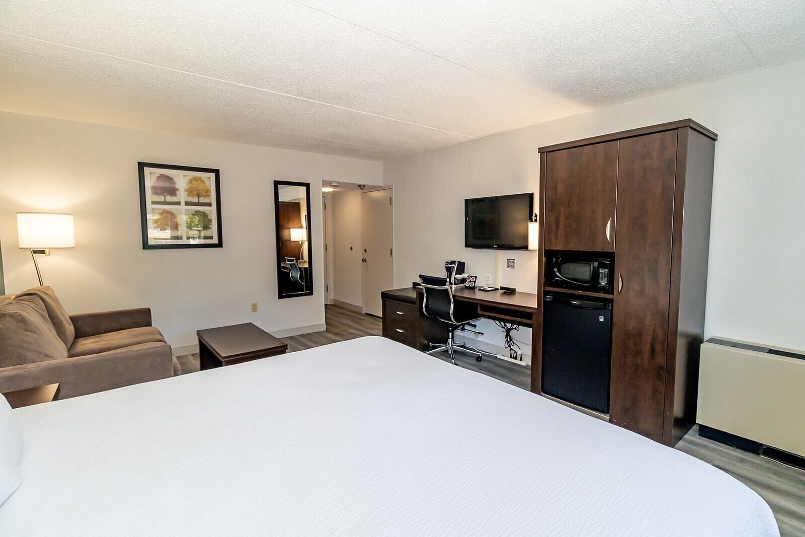 Habitación de hotel con una cama grande, un escritorio con computadora, televisión y minibar.