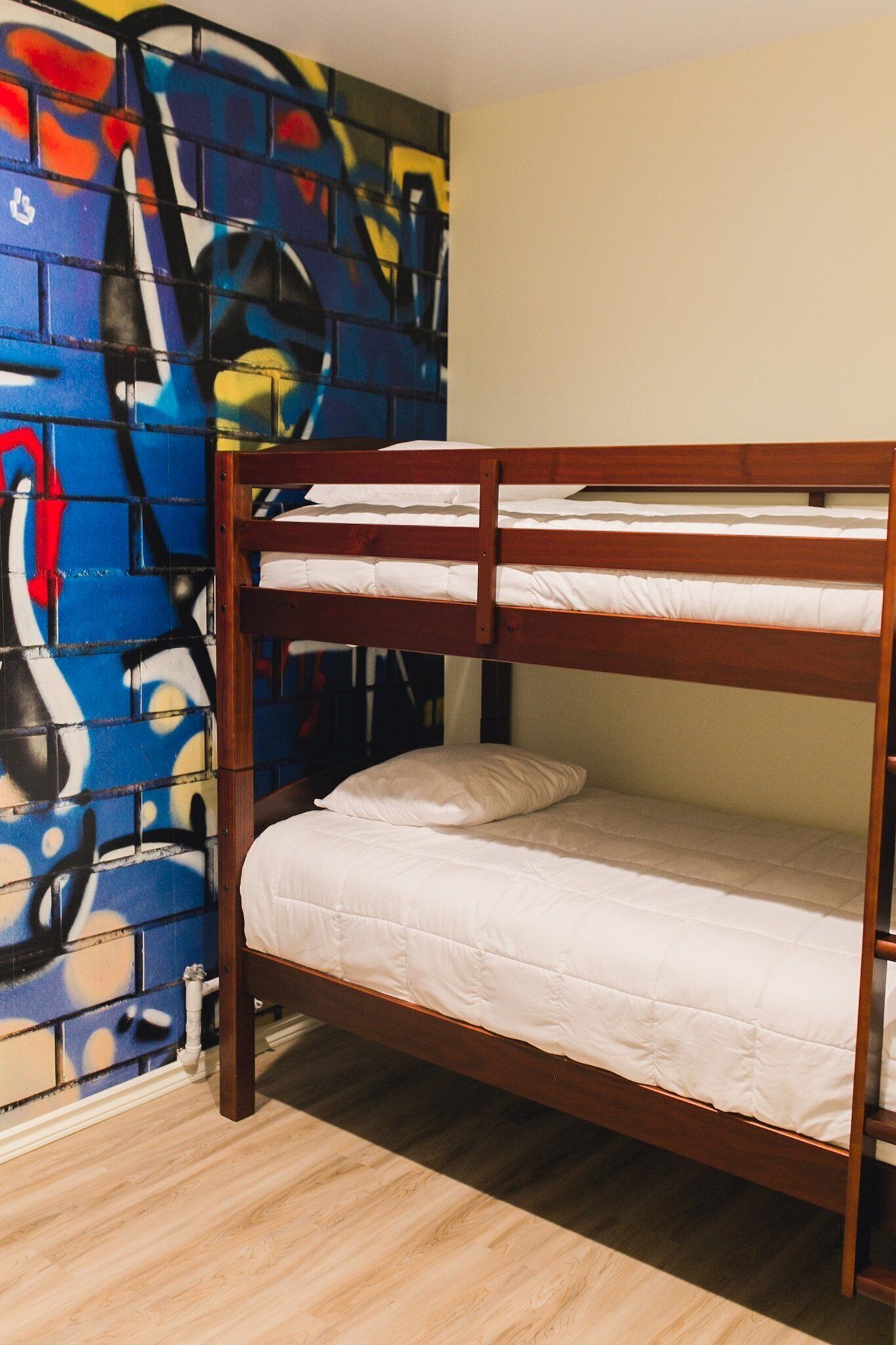 A bunk bed with white bedding, a wooden frame, and a colorful abstract mural on the adjacent wall.